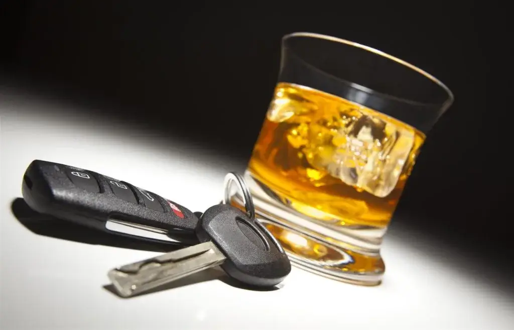 A glass of whiskey with ice next to a set of car keys, symbolizing the dangers of drunk driving.