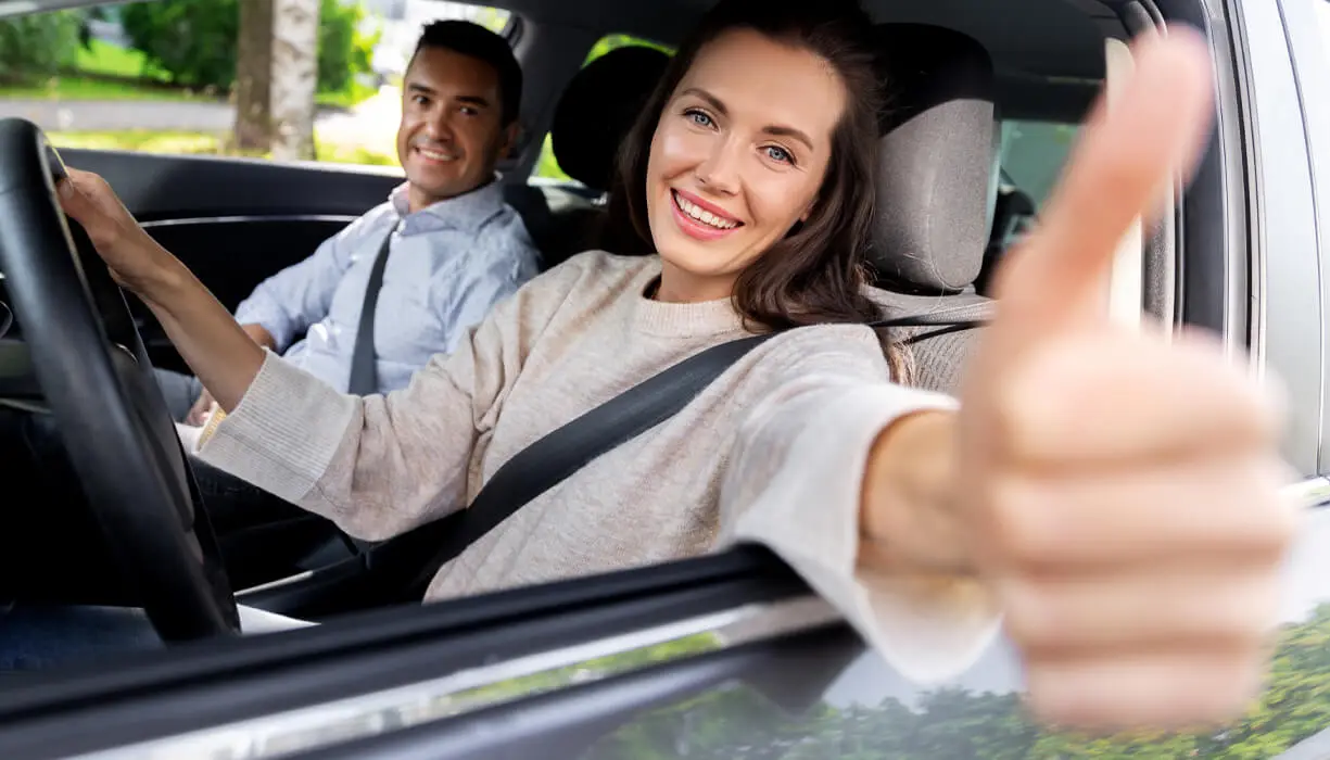 Couple in car, smiling and giving a thumbs up after getting the right insurance coverage from Breathe Easy Insurance