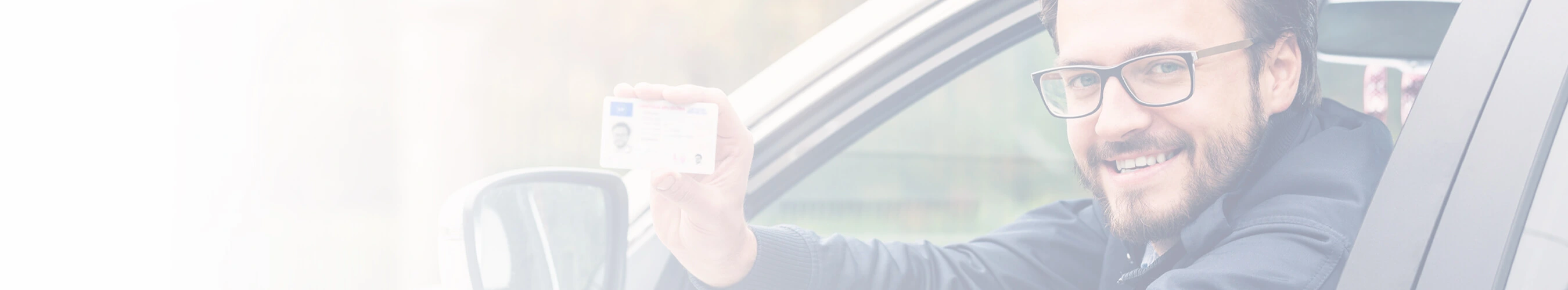 Smiling man holding up his driver’s license while seated in a car